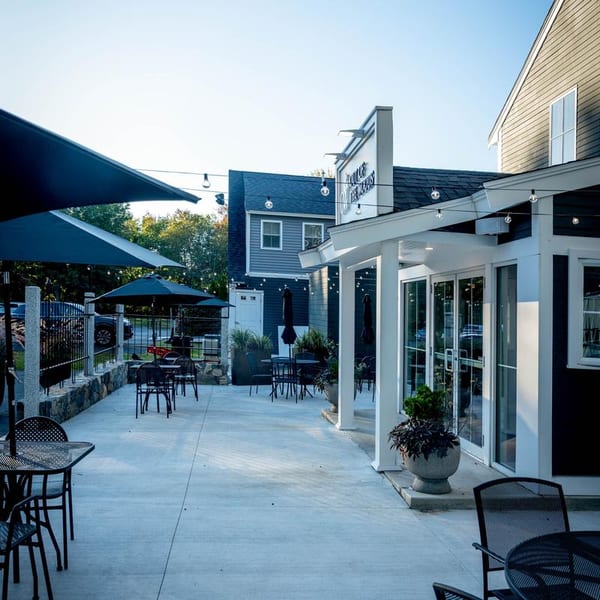 Outdoor patio dining area with black tables, chairs, umbrellas, and string lights at dusk.