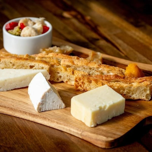Artisanal cheeses, sliced crusty bread, and fruit garnish arranged on a wooden serving board.