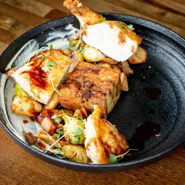 Roasted chicken pieces, a savory bread pudding, and brussels sprouts on a dark plate.