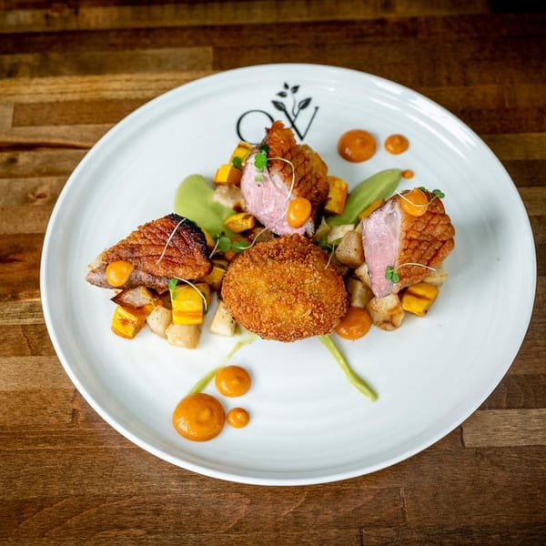 Seared duck breast, a fried croquette, and vegetables with sauces on a white plate.