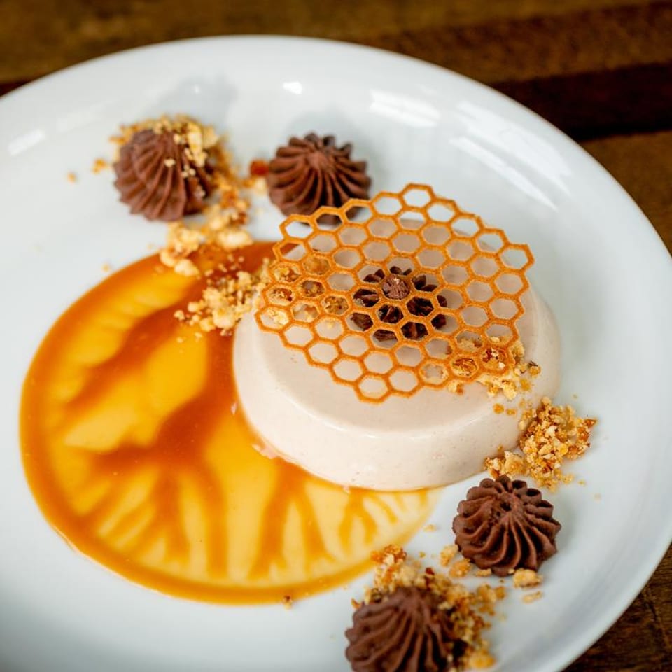 Elegant dessert with panna cotta, caramel, chocolate swirls, crushed nuts, and a honeycomb crisp.