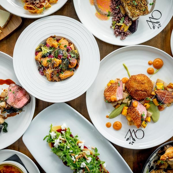 Overhead view of multiple gourmet dishes, including meat, pasta, and salad, on white plates.