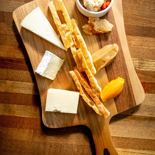 Cheese board with various cheeses, breadsticks, honey, and fruit paste on a wooden surface.